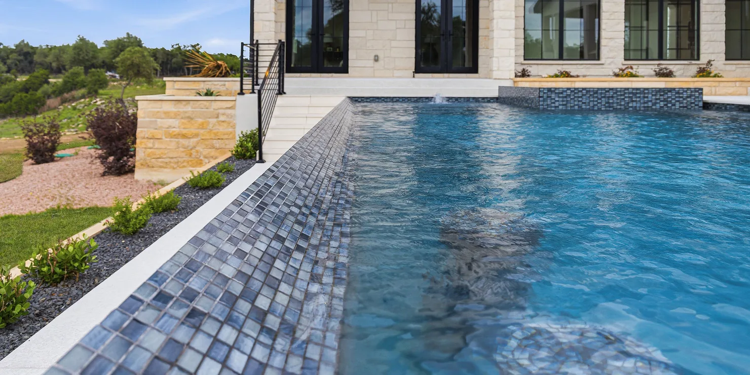 Modern infinity-edge pool with dark mosaic tile and clear blue water
