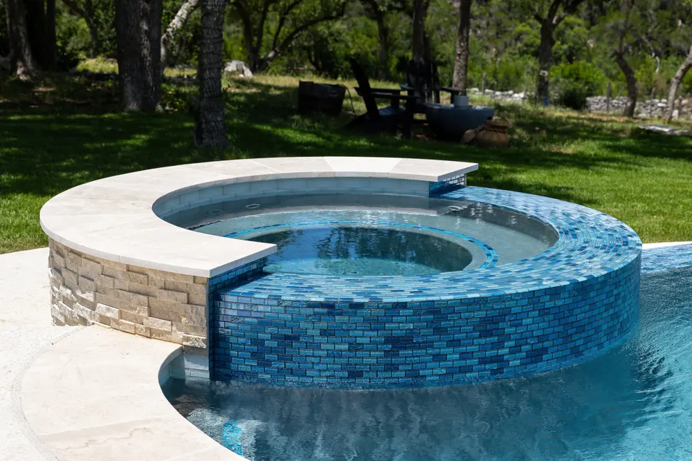 Circular raised spa with blue tile spillway added in a wooded backyard