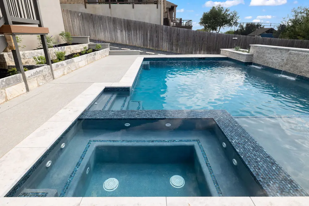 Resurfaced pool with crisp blue water and a stone spillway wall