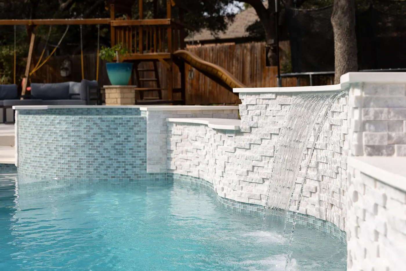 Stacked-stone waterfall feature flowing into a renovated backyard pool in San Antonio